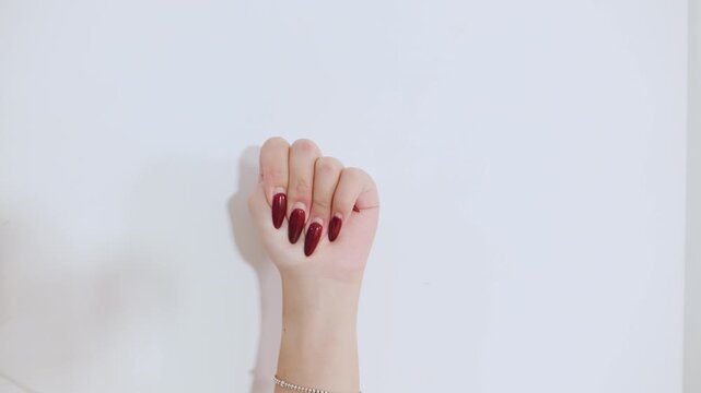 A womans hand showing four fingers folding over the thumb, the violence at home, signal for help stands out against a plain white wall, highlighting the artistry of nail design.
