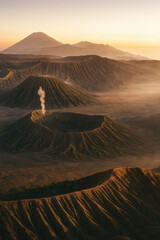 Aerial sunrise over volcanic calderas; ridges glow in golden haze, plume rising—epic landscape, adventure travel, generative AI