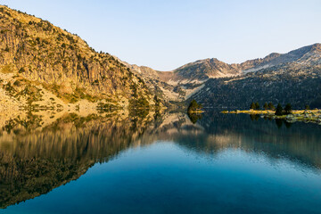 Fototapeta premium Panoramic view of Lake Aubert at sunrise, reflecting the mountains of the Néouvielle Nature Reserve