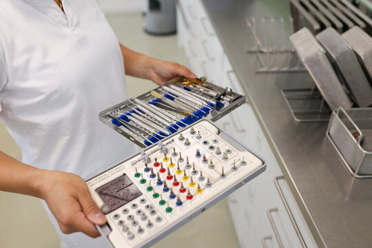 Hands of a dentist assistant carrying trays with cleaned drills and other tools.