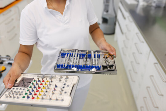 Hands of a dentist assistant carrying trays with cleaned drills and other tools.