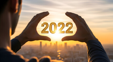 Hands framing golden 2022 year against vibrant sunset cityscape symbolizing future success