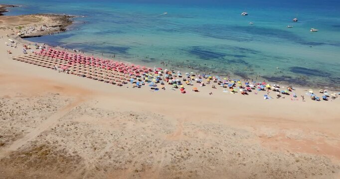 Aerial view of Macari Beach located near San Vito Lo Capo, in province of Trapani, Sicily, Italy. Many vacationers with umbrellas bathing in the clear, turquoise sea. There's a beautiful beach club.
