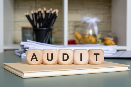 wooden cubes with word AUDIT on office desk with stationery and documents in background