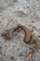 Old rusty horseshoe lying on sandy ground, close-up of corroded metal object partially buried in sand.