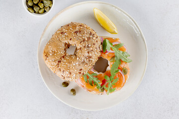 Bagel with salmon, cream cheese, cucumber and arugula on white background. Top view. 
