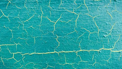 Close-up of vibrant turquoise paint with yellow cracks, creating a distressed abstract texture background
