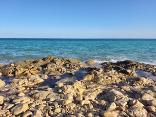 calm azure waters and sunlit stones scene, peaceful seaside landscape with smooth rocks and serene