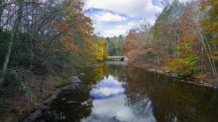 Fototapeta premium Scenic autumn view of a serene river reflecting colorful trees under a cloudy sky