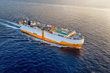Aerial view of a RORO car and vehicle transporter ship sailing with speed over the ocean during sunset