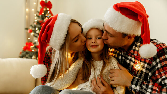 Mother, father, and daughter sitting together in Santa hats, parents kissing their smiling child on the cheeks, celebrating Christmas with warmth, joy, and love at home.
