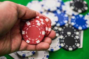 Naklejka premium Hand holding red poker chips at casino table.