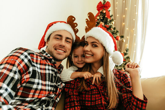 Christmas family. Father, mother, and daughter posing together in festive outfits, parents in Santa hats and child with reindeer antlers, festive decorated home sharing love and holiday atmosphere.