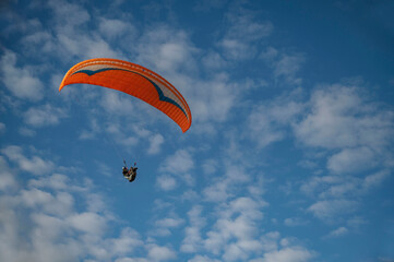 Oludeniz, Turkey. A close-up of a paraglider's orange parachute and a paraglider in flight against a cloudy sky.