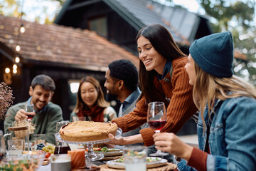 Happy woman serving pie while celebrating Thanksgiving with her friends on patio.