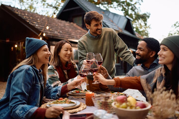Happy friends toasting with wine while gathering for lunch on patio in autumn.