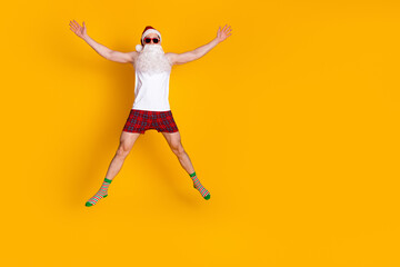 Playful Santa jumps in pajama shorts and hat against bright yellow background for festive holiday energy