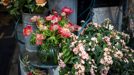 Red anemones and buttercups in a round glass vase on a metal chair, with a bouquet of orange roses for interior decoration on special occasions like weddings, dates, and funerals.