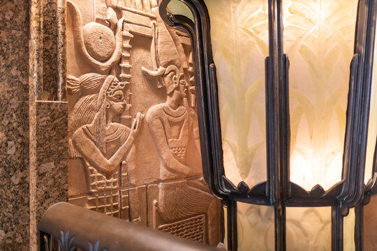 London, UK, December 4, 2024: The Harrods. Close-up of an art deco interior detail, showing a carved relief with egyptian-style figures next to a decorative patterned lamp.