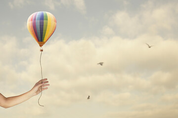 Hand holding a small hot air balloon in the sky with clouds and birds