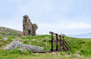 Old stone ruin and wooden bridge in a grassy field on Iona near the Isle of Mull, Scotland. Historic landmark surrounded by wild nature.