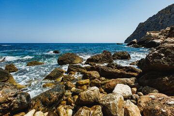 Crystal clear waves lap against rugged rocks on a sunny day at the serene coastal shoreline