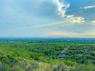 Obraz premium Expansive green landscape under a cloudy sky with rays of sunlight breaking through in a peaceful rural setting
