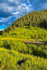 Obraz premium Captivating mountain landscape with lush greenery and a serene river under a vibrant sky in the late afternoon