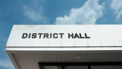 District hall word sign displayed on building facade with clear blue sky, representing a government office for local administration, community services, and civic engagement.