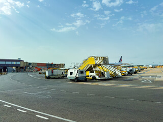 Busy airport terminal with bright yellow ground support vehicles preparing for the day ahead under a clear sky