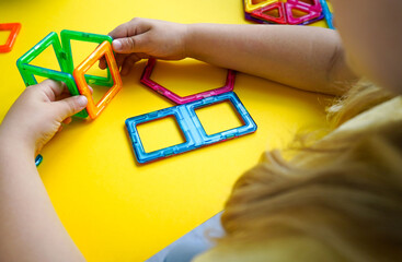 A colorful collection of magnetic geometric shapes is being transformed by a child into creative...