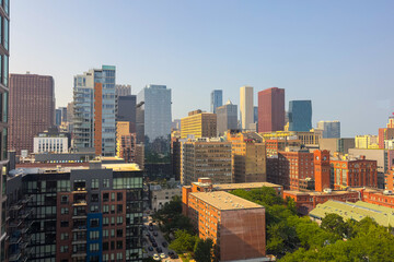 City skyline at midday showcasing modern skyscrapers and historic buildings under a clear blue sky filled with sun