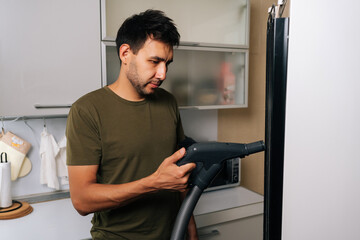 Side view of cleaning company worker using vacuum cleaner to remove dust and debris from refrigerator coils, performing essential maintenance for optimal cooling efficiency and energy saving