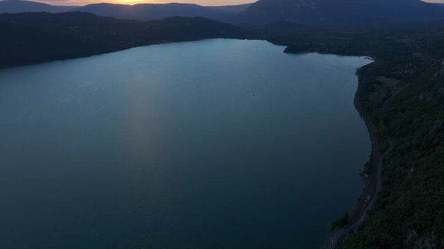  Lake surface reflecting the sunset sky. Calm summer weather and mountain silhouettes around Lac du Bourget in southeastern France.