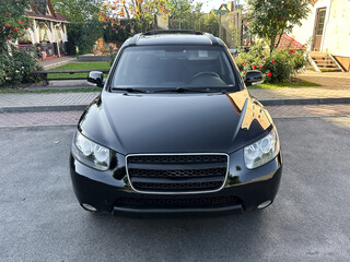 A sleek black SUV parked on a quiet street surrounded by green trees and blooming flowers on a sunny day, showcasing its polished exterior and bold design
