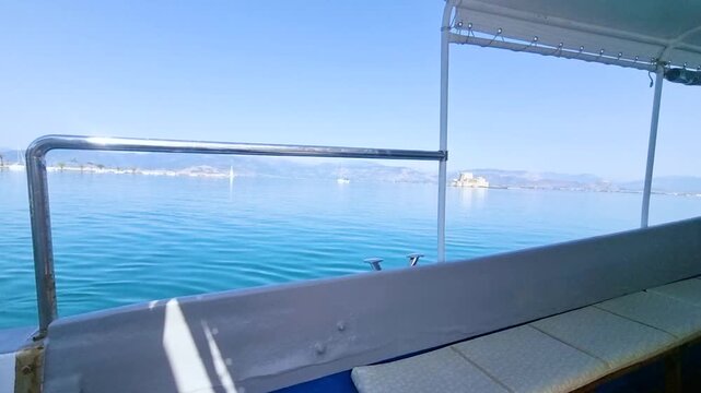 Nafplion Bay with turquoise water. View from the boat, the promenade with cafes and palm trees, yachts at the piers, hills on the background, clear day.