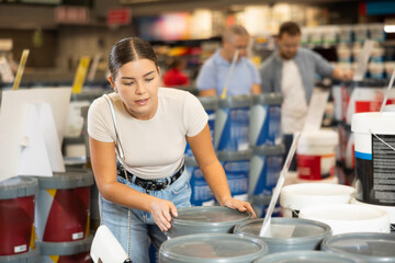 Girl examine bucket of paint and buys, collect necessary supplies in store for apartment renovation...