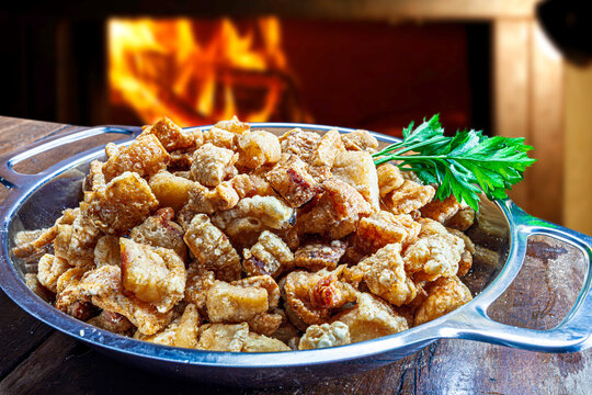 pork rinds (torresmo) fried in ceramic bowl on rustic wooden table in restaurant.