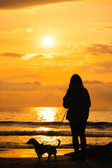 Woman walking dog on beach at sunrise