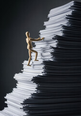 Wooden mannequin climbing a gigantic mountain of paperwork and documents, a concept of excessive work and overwhelming bureaucracy.