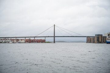 Stavanger, Norway, modern suspension bridge spans a body of water, with residential buildings and a ferry visible on the right side