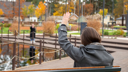 Woman Waving to Friend Across Park Lake on a Sunny Autumn Day Surrounded by Colorful Trees