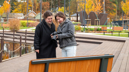 Two Friends Share a Moment in a Park While Reviewing Photos on a Camera During Fall
