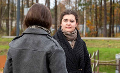 Two Women Having a Serious Conversation Outdoors in a Park During Autumn With Fallen Leaves Around Them