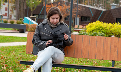 Young Woman Examines Camera While Sitting on a Park Bench During Autumn