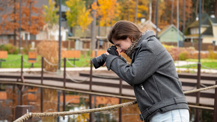 Young Woman Capturing Autumn Scenery With Camera Near a Tranquil Lake in a Forest Park Setting