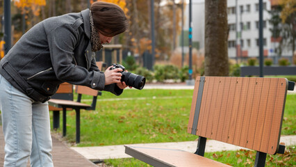 Woman Capturing Unique Photographs of an Empty Park Bench on a Cool Autumn Day in the City