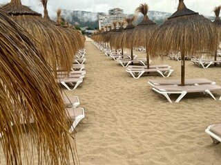Straw umbrellas and beach sunbeds on sand, Cloudy overcast day at the empty sea beach. Summer vacation is over. off season, no people