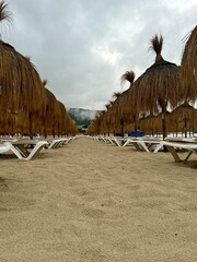 Straw umbrellas and beach sunbeds on sand, Cloudy overcast day at the empty sea beach. Summer...