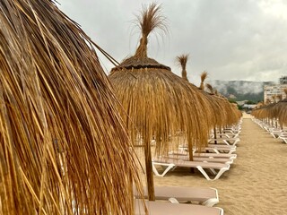 Straw umbrellas and beach sunbeds on sand, Cloudy overcast day at the empty sea beach. Summer vacation is over. off season, no people